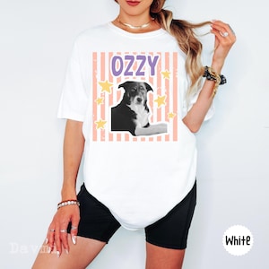 Peut inclure: Un t-shirt blanc &agrave; manches courtes avec une impression graphique d'un chien noir et blanc. Le motif comprend le texte OZZY en lettres violettes, sur un fond de rayures verticales p&ecirc;che et d'&eacute;toiles jaunes dispers&eacute;es sur le devant.