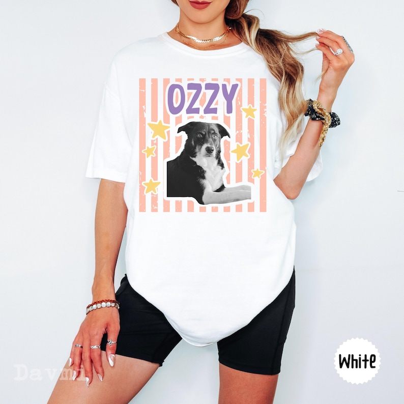 Peut inclure: Un t-shirt blanc &agrave; manches courtes avec une impression graphique d'un chien noir et blanc. Le motif comprend le texte OZZY en lettres violettes, sur un fond de rayures verticales p&ecirc;che et d'&eacute;toiles jaunes dispers&eacute;es sur le devant.