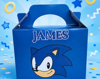 May include: A blue cardboard party favor box with a handle, featuring a graphic of the character Sonic the Hedgehog and the name JAMES printed in white letters on the front. The box has a smooth finish and a rectangular shape with a top handle.