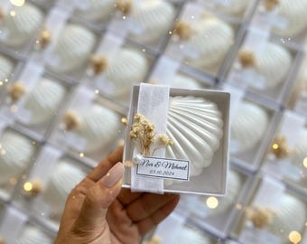 Puede incluir: Jabones blancos en forma de concha en cajas transparentes, perfectos para una boda o evento. Cada jabón está adornado con un pequeño acento floral y una etiqueta que dice "Nur & Mehmet 03.10.2024".