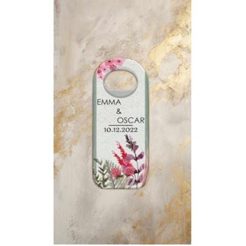 May include: A decorative door hanger with a floral design and the names "EMMA & OSCAR" along with the date "10.12.2022". The top features a circular opening, and the bottom has a watercolor-style floral arrangement in shades of pink and purple.