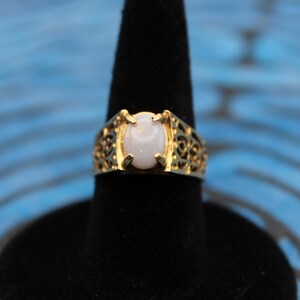 May include: A gold ring with an oval-shaped white opal gemstone set in a filigree design.