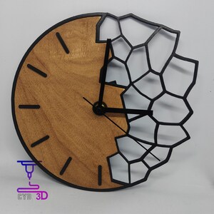 Può includere: Un orologio da parete rotondo con quadrante in legno e lancette nere. Il quadrante è parzialmente coperto da un design geometrico nero. L'orologio ha indicatori delle ore neri e il testo "CYD 3D".