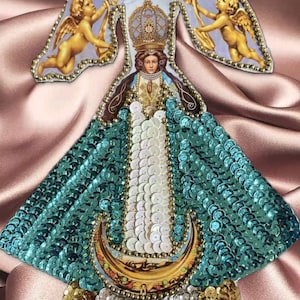 May include: A religious icon featuring a woman with a crown, adorned with teal sequins and gold accents. Two cherubs flank the figure, and the image is set against a pink satin background.