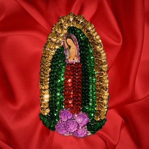 May include: A colorful, beaded image of the Virgin Mary, with gold, green, red, and purple sequins. The image is surrounded by a gold border.