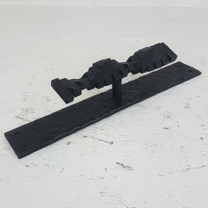 Puede incluir: Pomo de puerta de metal negro con acabado texturizado. El pomo tiene forma de una serie de cuadrados conectados y está montado en una placa de metal negro.