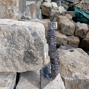 May include: A metal door handle shaped like a stack of dice. The handle is mounted on a square metal plate and is attached to a wall.