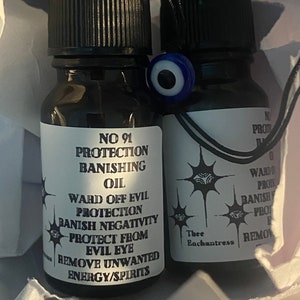 Puede incluir: Dos pequeñas botellas de vidrio con tapas negras y etiquetas blancas. Las etiquetas tienen texto negro que dice "NO 91 PROTECTION BANISHING OIL WARD OFF EVIL PROTECTION BANISH NEGATIVITY PROTECT FROM EVIL EYE REMOVE UNWANTED ENERGY/SPIRITS" y "Thee Enchantress". Las botellas están sobre una superficie blanca.