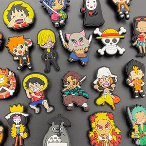 May include: A selection of colourful anime-themed shoe charms. The charms depict various characters with distinct designs and vibrant colours, including characters with yellow hair, straw hats, and swords. The charms are made of rubber and are designed to be attached to shoes.