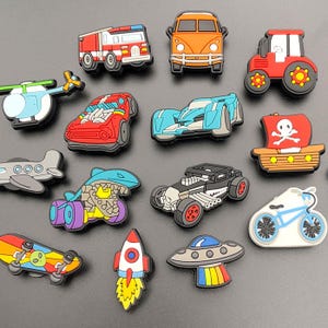 May include: A selection of colourful shoe charms in a cartoon style, depicting different vehicles and objects. Includes a fire engine, orange car, tractor, race cars, pirate ship, aeroplane, skateboard, rocket, and a UFO.