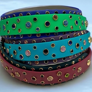 May include: Five colorful leather collars with gold accents and various colored rhinestones. The collars are stacked on top of each other.
