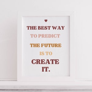 May include: White framed print with the text "The best way to predict the future is to create it." in brown, pink, and orange lettering with a small heart at the top.