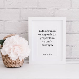 May include: White framed print with a quote by Anais Nin: "Life shrinks or expands in proportion to one's courage."