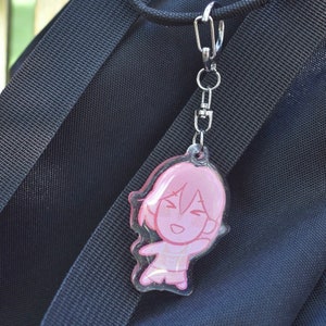 May include: A pink and white cartoon character keyring with a smiling face. The keyring is attached to a silver chain.