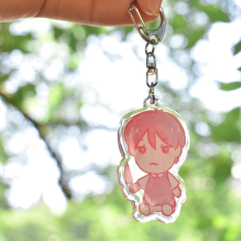 May include: A pink and white anime character keychain with a silver chain. The character is holding a knife and has a pink and white glitter finish.
