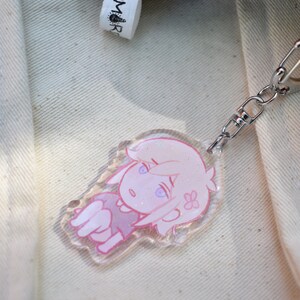 May include: A pink and white anime character keyring with glitter accents. The keyring is attached to a silver chain.
