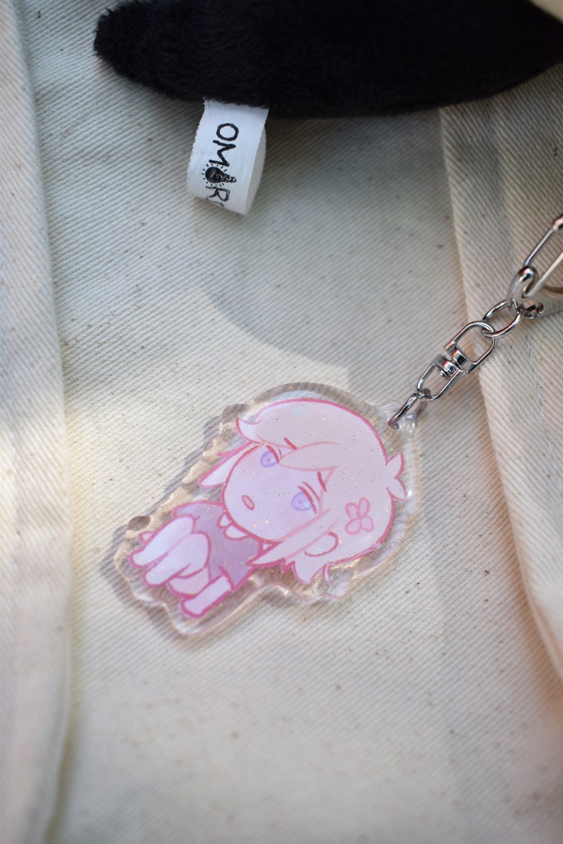May include: A pink and white anime character keyring with glitter accents. The keyring is attached to a silver chain.
