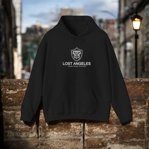 Puede incluir: Sudadera con capucha negra con un logotipo blanco que presenta un escudo con manillares cruzados y el texto "Riders Los Angeles Fixed Gear Cycling".