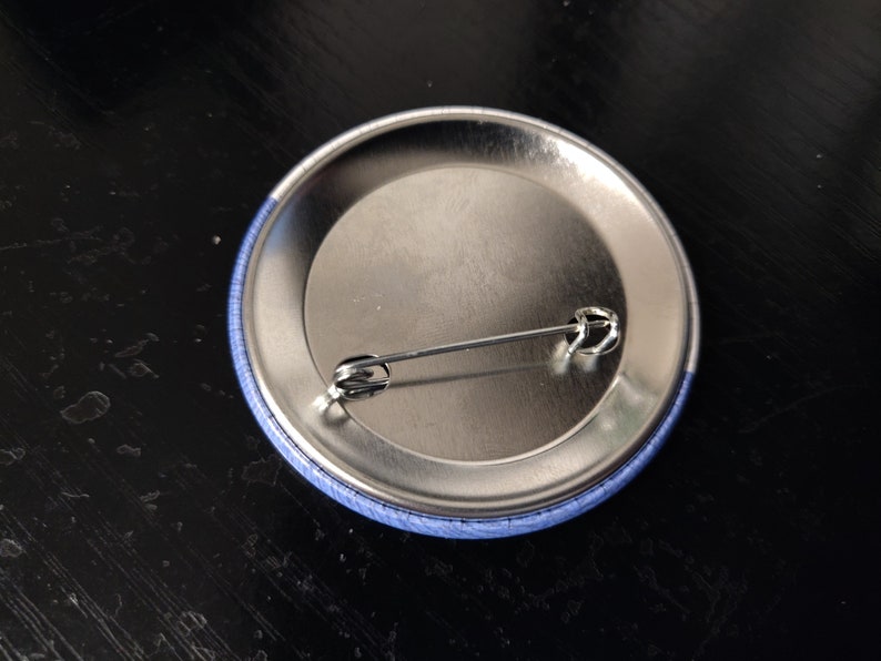 May include: The back of a blue button with a silver pin attached.