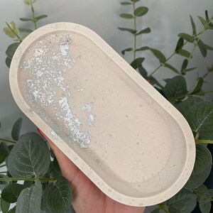 May include: A light beige oval tray with a silver glitter design. The tray is made of resin and has a smooth, glossy finish.