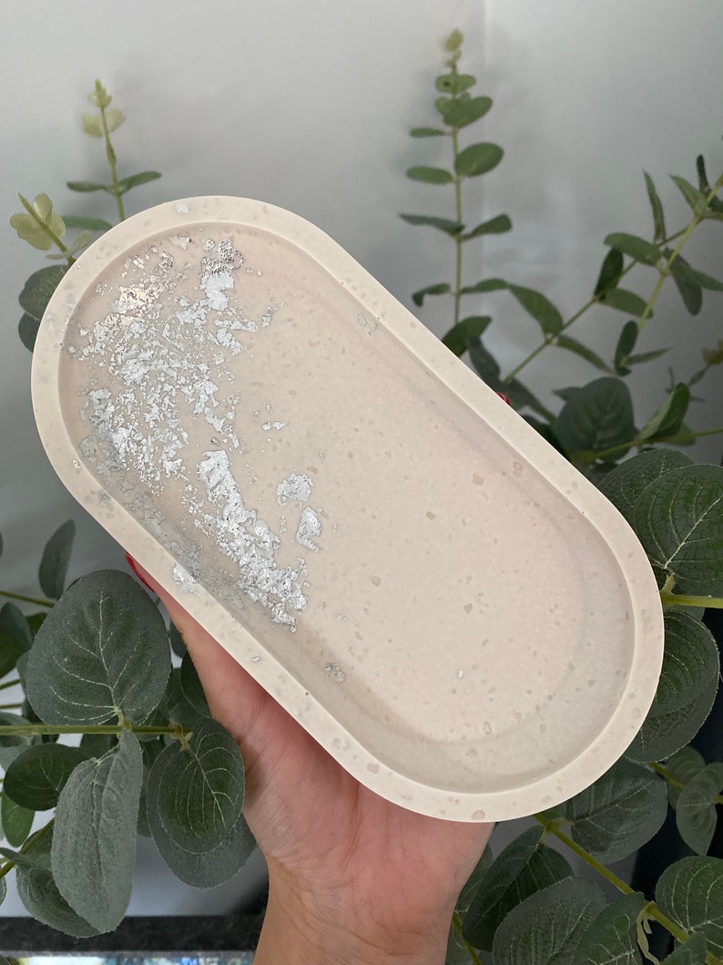 May include: A light beige oval tray with a silver glitter design. The tray is made of resin and has a smooth, glossy finish.