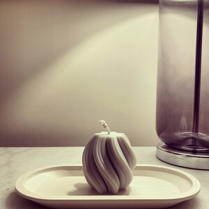 May include: A white, swirl-shaped candle sits on a white oval tray. The candle is on a white surface.