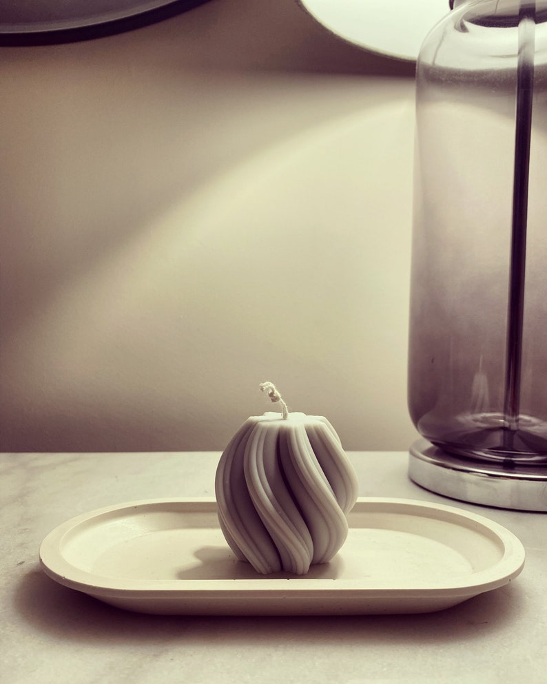 May include: A white, swirl-shaped candle sits on a white oval tray. The candle is on a white surface.