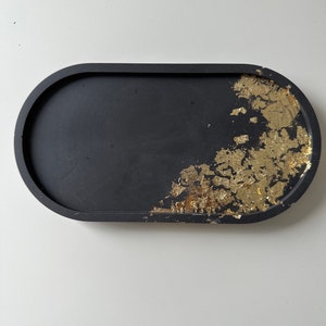 May include: A black oval tray with gold leaf accents. The tray is made of resin and has a smooth, glossy finish.