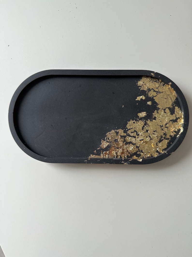 May include: A black oval tray with gold leaf accents. The tray is made of resin and has a smooth, glossy finish.