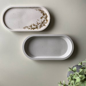 May include: Two oval-shaped concrete trays. One tray has a white background with gold leaf accents. The other tray is plain white.