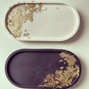 May include: Two oval-shaped trays with gold leaf accents. One tray is white and the other is black.