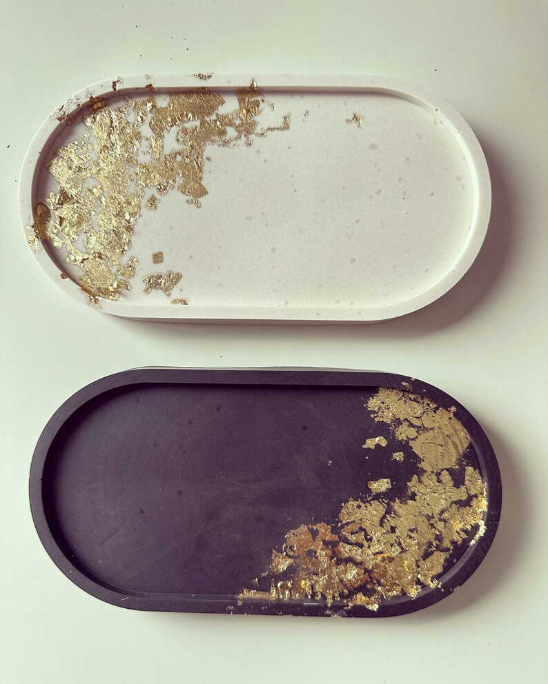 May include: Two oval-shaped trays with gold leaf accents. One tray is white and the other is black.