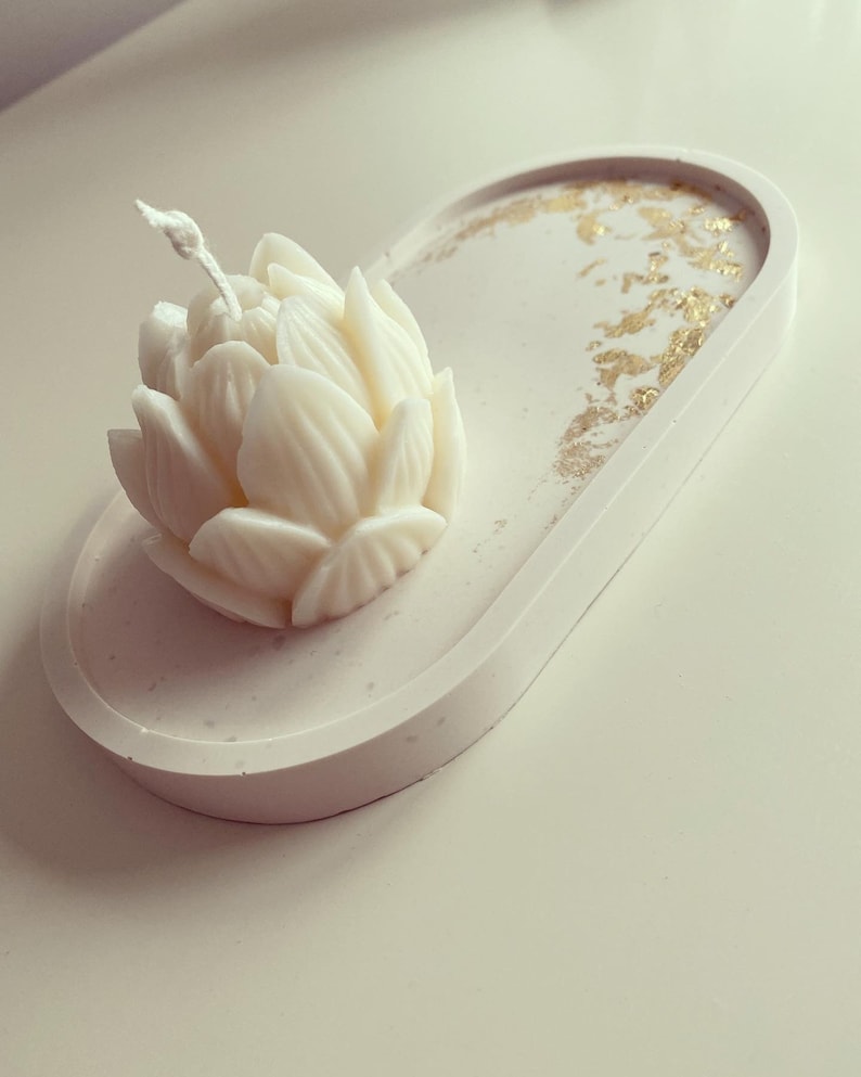 May include: A white ceramic tray with gold flecks and a white lotus flower candle in the centre.