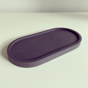 May include: A dark grey oval-shaped tray made of concrete. The tray has a smooth, slightly textured surface and a raised edge.