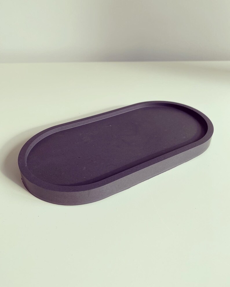 May include: A dark grey oval-shaped tray made of concrete. The tray has a smooth, slightly textured surface and a raised edge.