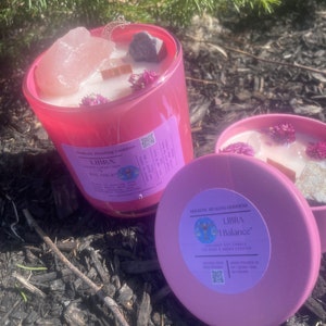 May include: Pink coconut soy candle with a Libra zodiac symbol and the text "I Balance" on the label. The candle is decorated with crystals and dried flowers.