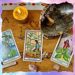 May include: A wooden surface displays tarot cards, a lit candle, a seashell, crystals, and a piece of wood. The tarot cards are labeled "Two of Swords", "Eight of Pentacles", and "XI Justice". The candle is in a gold tin and has dried flowers.