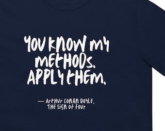 Pode incluir: Camiseta azul marinho com texto branco que diz "You know my METHODS. APPLY THEM." O texto está escrito à mão. Abaixo do texto, uma citação de Arthur Conan Doyle, "The Sign of Four."
