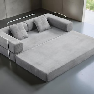 May include: A modern gray sectional sofa with a pull-out chaise lounge. The sofa features a corduroy-like texture and includes two square throw pillows. The design incorporates metal armrests for a minimalist aesthetic.