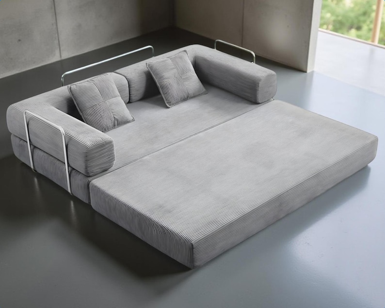 May include: A modern gray sectional sofa with a pull-out chaise lounge. The sofa features a corduroy-like texture and includes two square throw pillows. The design incorporates metal armrests for a minimalist aesthetic.