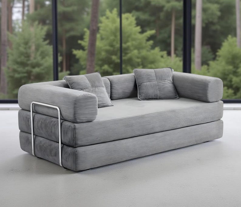 May include: A modern gray sofa with a minimalist design. The sofa features a corduroy-like texture and includes two square throw pillows. The frame has a silver metal accent. The sofa is a stylish addition to any living space.