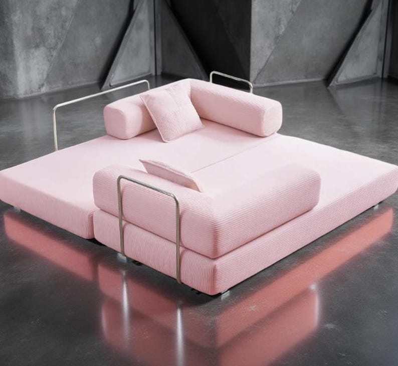 May include: A modern, modular sofa in a soft pink hue. The sofa features a low profile with a rectangular base and rounded bolster cushions. Silver metal armrests add a sleek contrast. Includes a small square pillow.