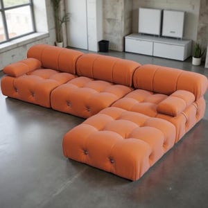 May include: An orange modular sofa with a tufted design. The sofa has a rounded shape and is composed of several connected sections, including an L-shaped configuration. The cushions are button-tufted, and the sofa is placed on a concrete floor.