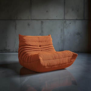 May include: An orange, low-profile lounge chair with a textured fabric. The chair has a rounded shape with a backrest and a seat, and is set against a concrete wall. The chair's design features horizontal, ribbed detailing.