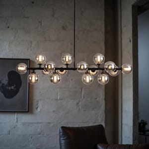 May include: A modern black chandelier with multiple spherical glass shades. The light fixtures are arranged horizontally, with each globe containing a warm light. The chandelier hangs from the ceiling in a room with a brick wall.