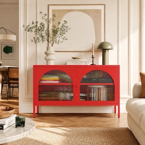 May include: A vibrant red cabinet with arched glass doors. The cabinet has a rectangular shape and sits on four thin legs. Inside, books and decorative items are visible. The cabinet is a modern piece of furniture.