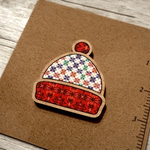 May include: A wooden ornament shaped like a winter hat with a red, white and blue patterned design. The hat has a small pom-pom on top.