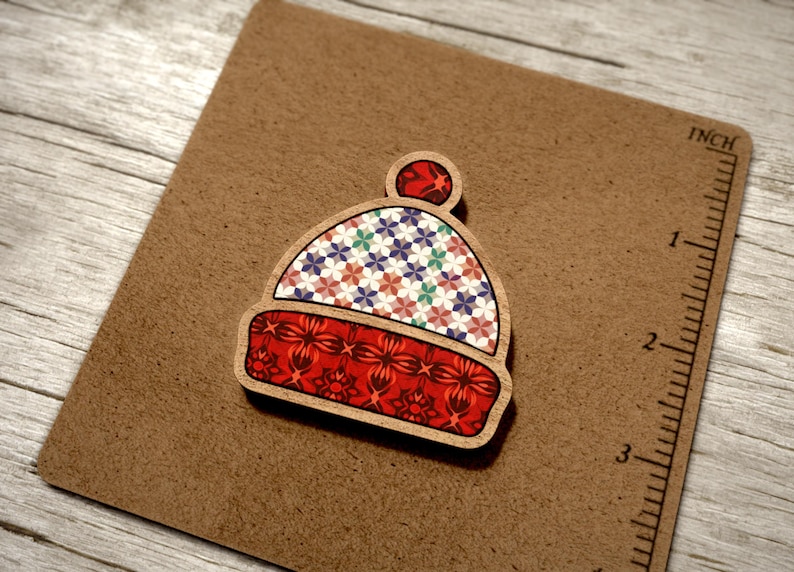 May include: A wooden ornament shaped like a winter hat with a red, white and blue patterned design. The hat has a small pom-pom on top.