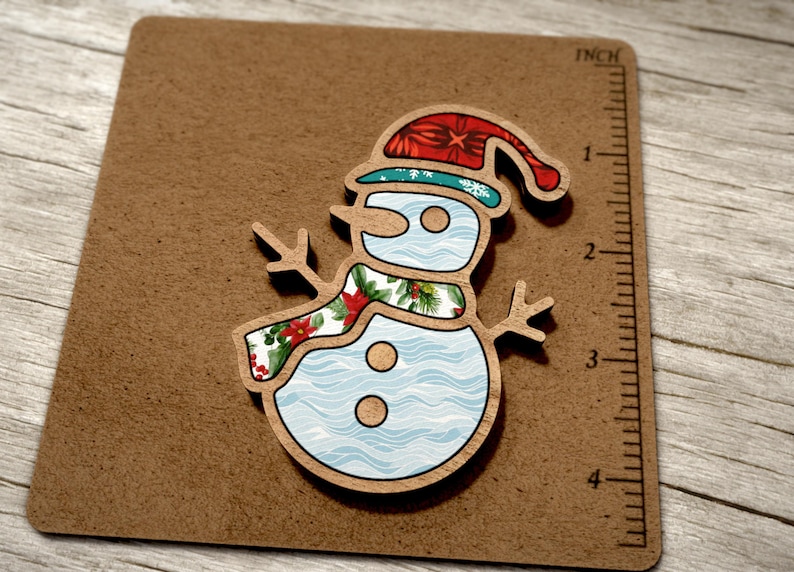 May include: A wooden snowman ornament with a blue and white patterned body, a red and green floral scarf, and a red hat with a white snowflake design.