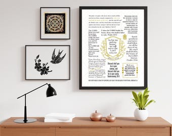 May include: Three framed art prints displayed on a wooden cabinet. The prints feature a black and white bird and floral design, a gold and black circular design, and a framed Bible verse with gold accents. A black desk lamp and a small potted plant are also present.